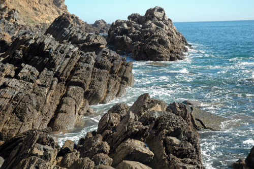 Black volcanic rock formations surrounded by coastal waves