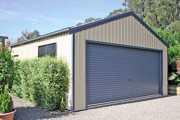 Cream double garage with blue roller door and trim in garden with shrubbery and potted plants