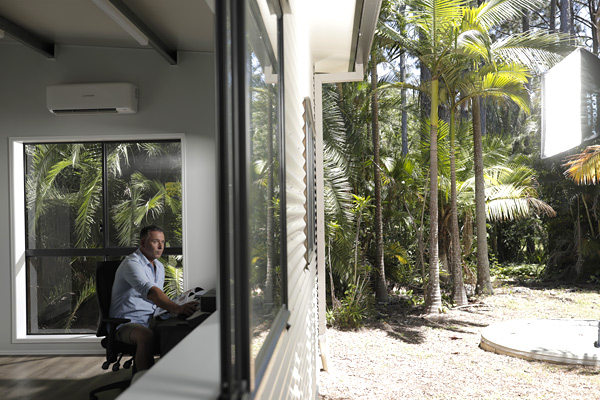 Home office viewed through the shed window showing man working at desk.