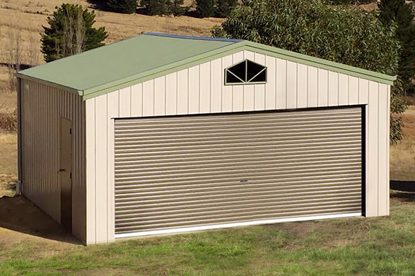 Cream shed with green roof, double roller door, side access door and barn window at top of gable