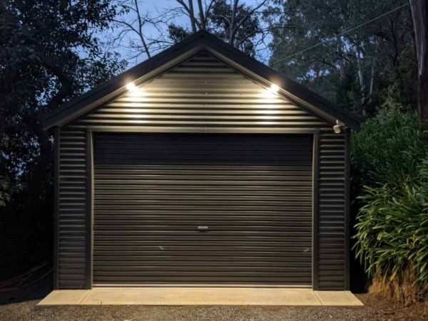 Gable roof garage with one roller door shot at night with two down lights illuminating the front