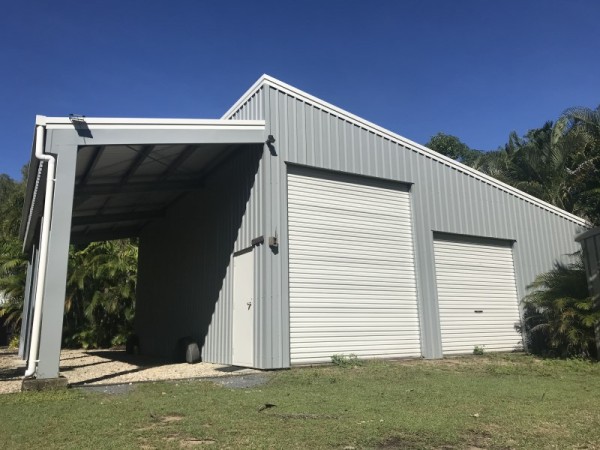 Skillion garage with open lean to on left side, two white garage doors on right side in grey cladding with white trim. 
